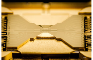 Close-up view of an Ion trap chip, which is a gold rectangle with two flat triangles pointing at each other.